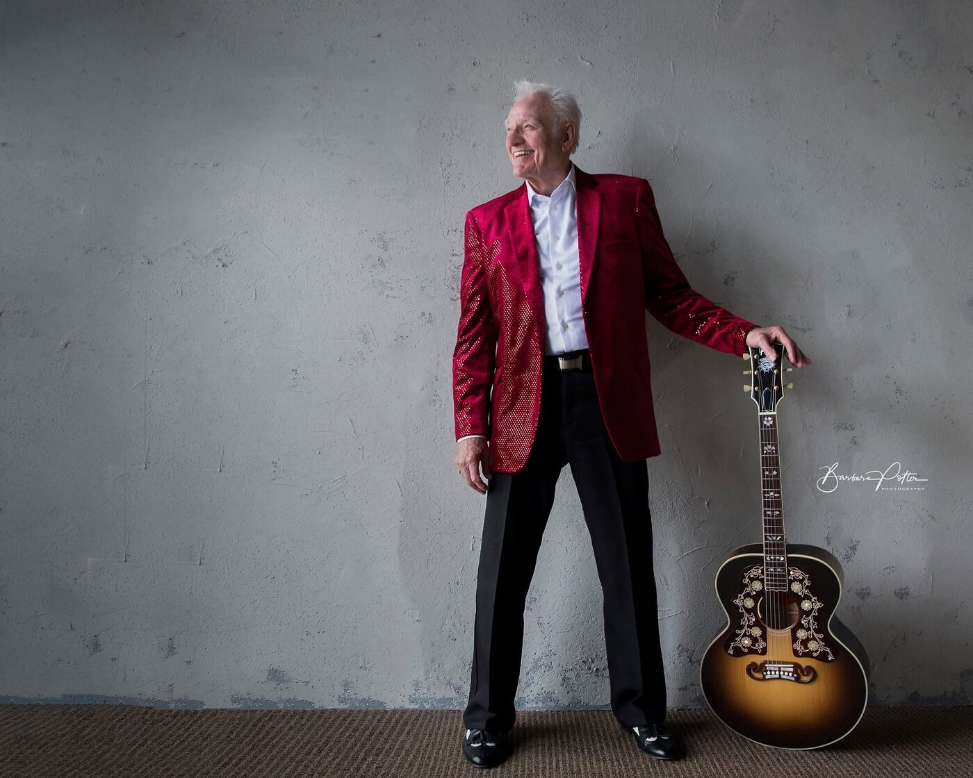 Jerry Foster in a red jacket standing with an acoustic guitar