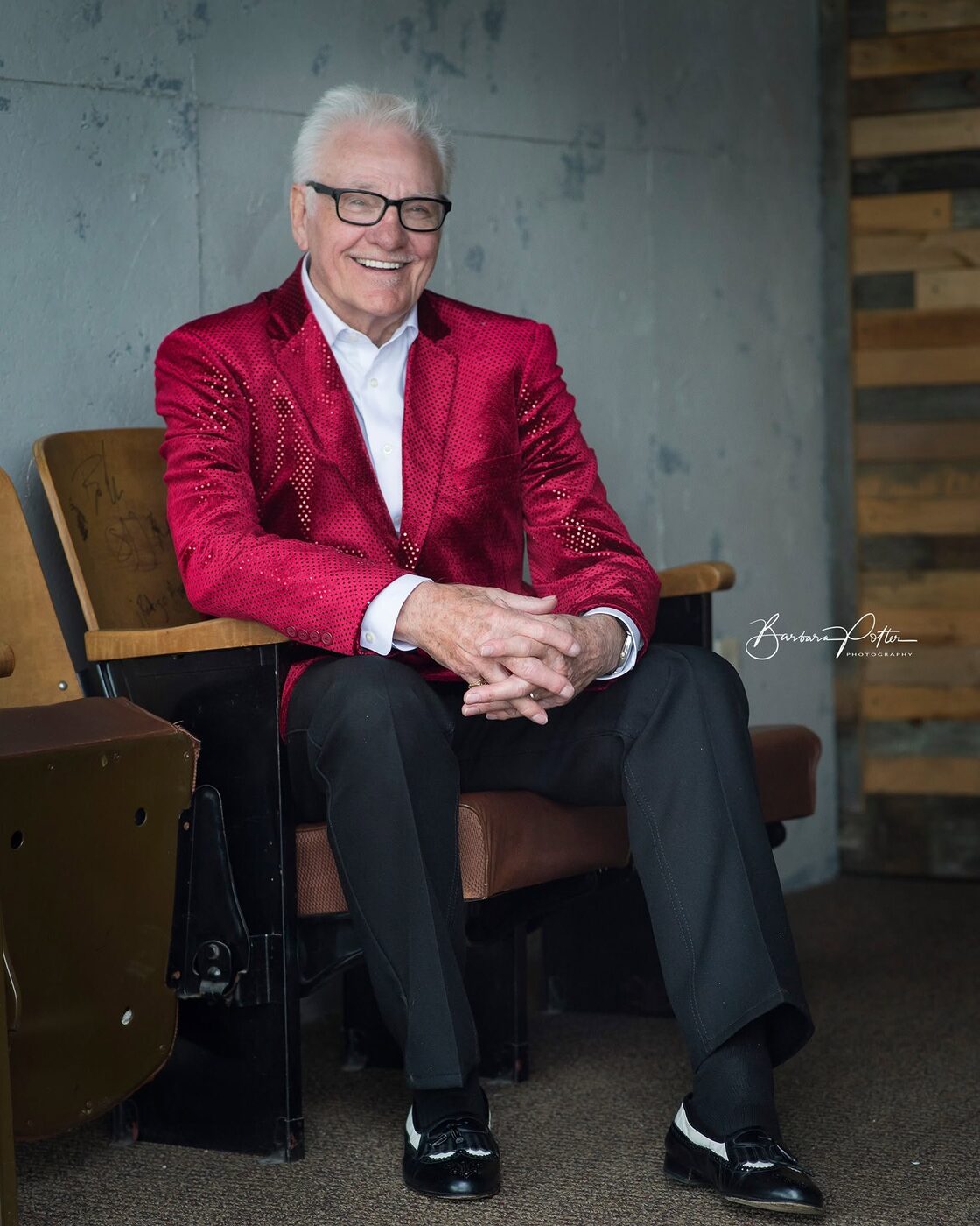 Songwriter Jerry Foster in a red jacket, seated in a theater chair