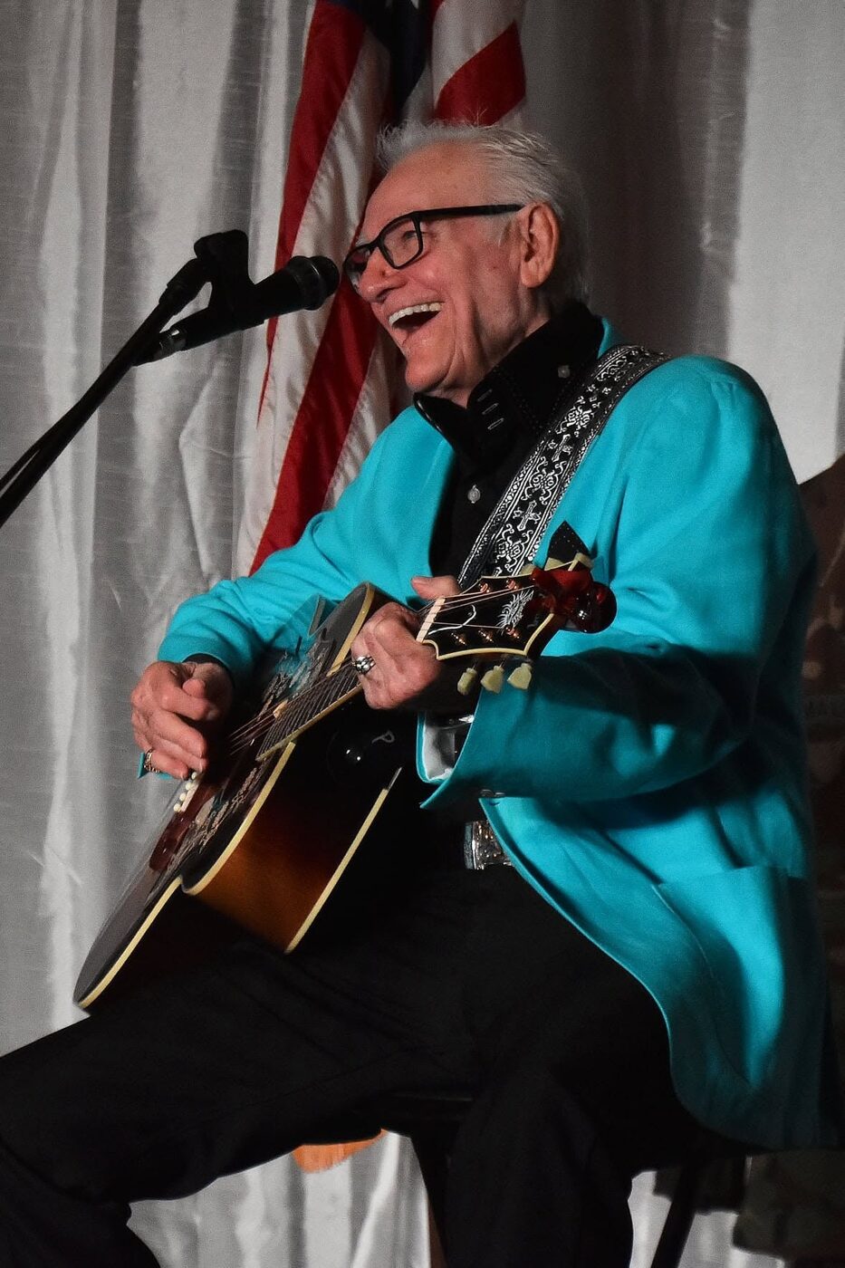 Jerry Foster laughing on stage in a turquoise jacket with guitar
